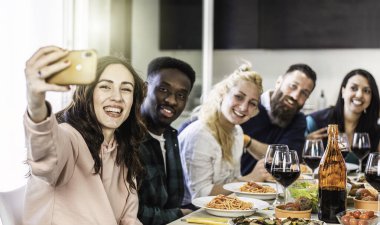 Multiethnic guys and women taking selfie for lunch in the home kitchen - Young friends having fun together in the apartment while eating delicious italian spaghetti with tomato sauce - Bright filter clipart