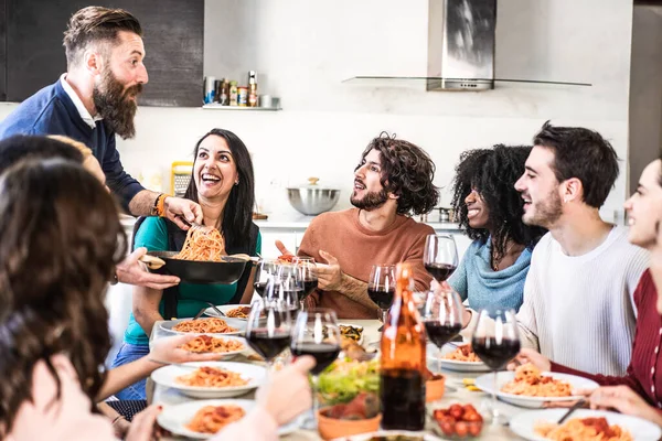 在一个令人惊奇的晚宴上 快乐的多种族朋友在家里吃着意大利面或番茄酱面条 喝着红酒 微笑的嬉皮士家伙为他的朋友们提供意大利面当晚餐 — 图库照片