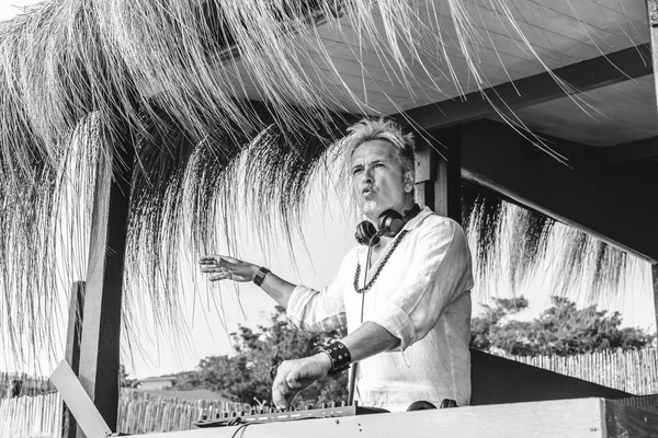 Disc jockey playing music for tourist people at club party outdoors on the beach - Dj wearing headphones at music live event - Live event, music and fun concept - Black and white editing