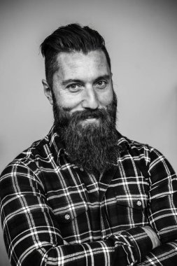 Sakallı bir adamın portresi ekose gömlek giyen ve kendine güvenen bir gülümseme. Siyah ve beyaz görüntü, minimalist bir stüdyo ortamında engebeli stil ve bireyselliği vurguluyor. Hippi hayatı.