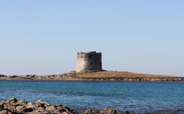Eski sahil gözlem kulesi Akdeniz 'in mavi sularıyla çevrili kayalık bir adada tek başına duruyor. Temiz gökyüzü ve sakin su, sahnenin sükunetini vurgular..