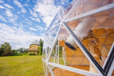 Ağaçlarla çevrili kubbeleri ve bulutlu gökyüzünün altındaki yeşil çimlerle gözlemevi manzarası.