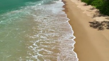 Havadan kumandalı insansız hava aracı güzel deniz dalgası ve kumsal sahili üzerinde uçuyor ve kamerayı eğiyor.