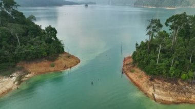 Hava aracı öne doğru uçuyor ve kamerayı kaldırarak Khao Sok Ulusal Parkı, Suratthani, Tayland gölü arasındaki dağın zirvesini gösteriyor.