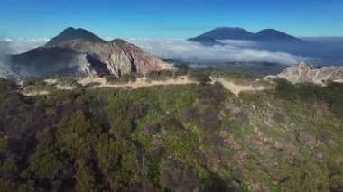 Gökyüzü görüntüsü bir ağacın yanından geçerken arkadaki Kawah Ijen yanardağını, Java 'yı, Endonezya' yı gösterir.