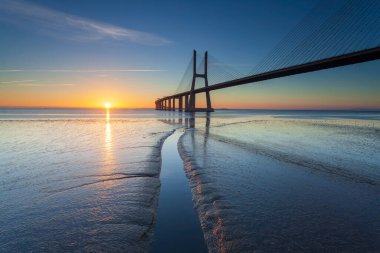 Lizbon nehrinde inanılmaz bir gün doğumu. Vasco da Gama Köprüsü bir dönüm noktasıdır ve dünyanın en uzun köprülerinden biridir. Şehir manzarası. Portekiz inanılmaz bir turistik yerdir.. 