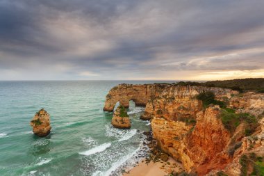 Gün batımında Algarve sahilinde manzara. Portekiz 'in güneyindeki plaj turistler için en iyi tatil yeridir. Uçurumlarda mağaraları olan deniz manzarası