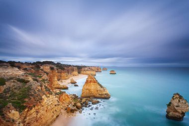 Gün batımında Algarve sahilinde manzara. Portekiz 'in güneyindeki plaj turistler için en iyi tatil yeridir. Uçurumlarda mağaraları olan deniz manzarası