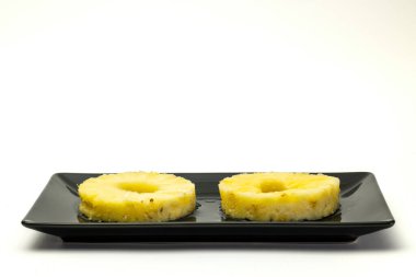 Two pineapple slices on a black plate.