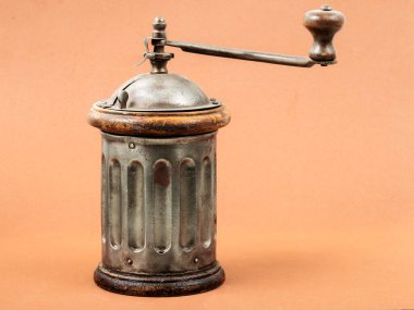 Vintage manual coffee grinder with a metal and wooden design on an orange background. clipart