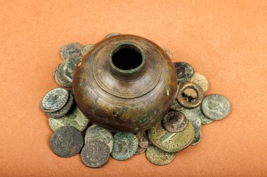 Antique bronze oil lamp surrounded by old Roman coins on a textured surface. clipart