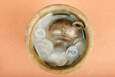 Ancient bronze pot filled with old coins and mist effect on an orange background. clipart