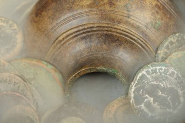 Close-up of an ancient bronze oil lamp surrounded by vintage Spanish coins with a smoky effect. clipart