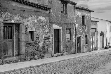 Köy sokaklarında yıpranmış duvarları ve ahşap kapıları olan eski taş bir ev..