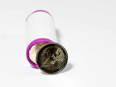 Beyaz arka planda paketlenmiş bir bozuk para rulosunun önünde duran iki euro..