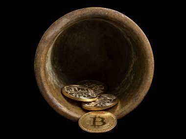 Golden bitcoin coins spilling from an antique bronze bowl on black background.
