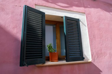 Pembe taştan bir duvarda koyu renk panjurlar olan bir pencere. Alcdia, Mallorca, İspanya. Bir Akdeniz ülkesinde dar, eski bir cadde. Ahşap kapılar, pencereler, ahşap panjurlar ve balkonlar. Eski Alcdia kasabası Mayorka 'nın kuzeyinde bir ortaçağ mücevheridir.