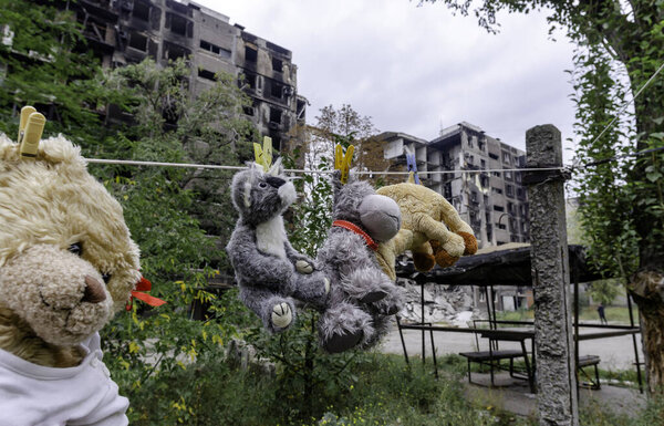 детские игрушки висят на веревке на фоне разрушенных сожженных домов войны на Украине с Россией