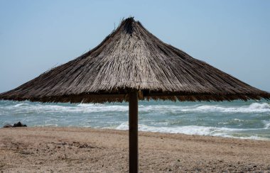 Açık bir günde boş bir deniz kıyısında saman plajı şemsiyesi.