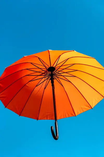 one orange umbrella flying in the wind against a blue sky