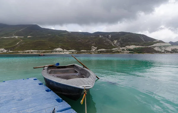 old boat near the shore of a mountain lake and high mountains and clouds without people