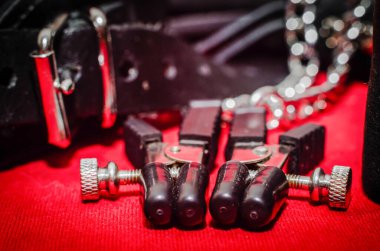 bdsm aksesuar insan tasması ve kırmızı arka planda metal zincirli aksesuar meme ucu tokası.