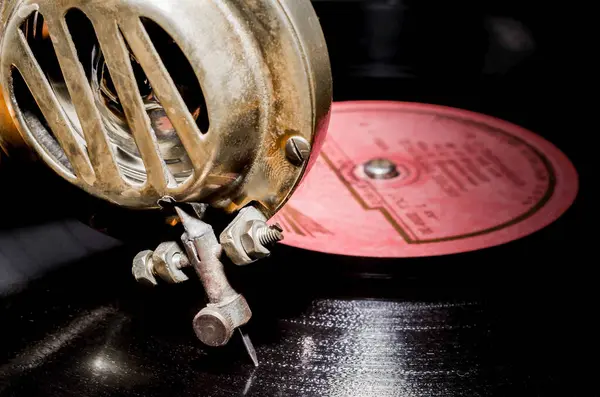 needle and a head of an old antique rarity gramophone made of yellow metal on a vinyl record with a red label close-up