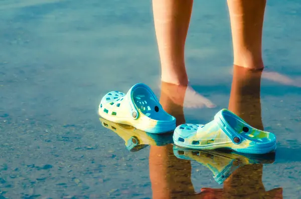 rubber slippers float in clear water next to female legs closeup