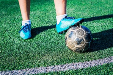 Yeşil futbol sahasında futbol topuyla mavi ayakkabılı genç bir futbolcunun bacakları.