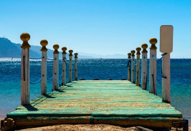sütun ve bir uyarı işareti mavi deniz ve dağlar denize karşı ahşap iskele
