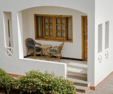 sandalye ve bir yuvarlak masa ve yakın yeşil bir çalı ile resort binasının Teras