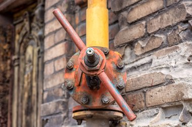 Kirli kırmızı gaz vanası. Eski bir evin duvarında sarı bir boru var.