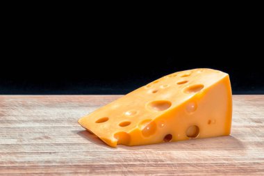 Üç köşeli sarı peynir renginde siyah bir arka planda tahta bir tahta üzerinde.
