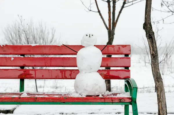 creepy snowman on a red bench in a snowy deserted park