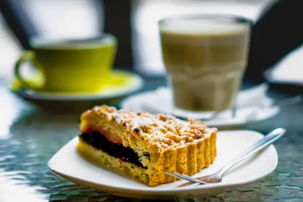 triangular piece of poppy pie and a fork with powdered sugar on a background of a transparent glass with white coffee and a yellow cup