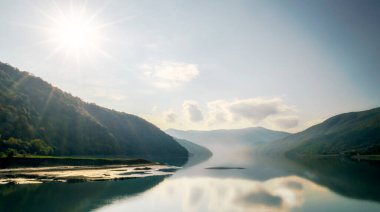 Gürcistan 'daki güneş, gökyüzü ve bulutların arka planında yeşil orman ve gölle sonbahar manzarası