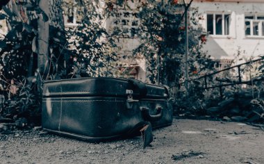 Ukrayna 'da savaş sırasında terk edilmiş bir şehirde yıkılmış bir evin arka planında eski bir bavul.