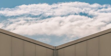 Modern bej bir binanın köşesi ve beyaz bulutlu mavi bir gökyüzü.