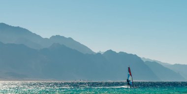 windsurfer rides in the Red Sea against the backdrop of high rocky mountains in Egypt