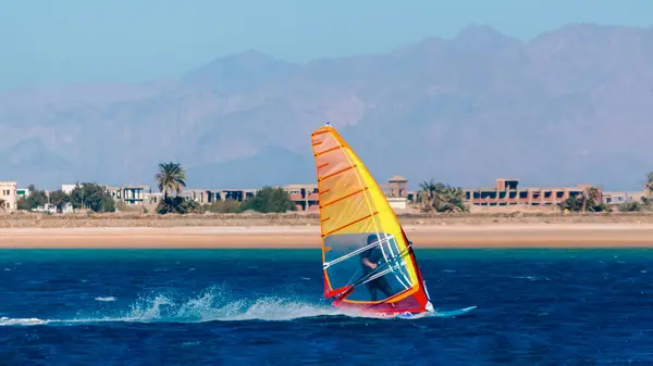 stock image windsurfing in the blue water on the background of the beach with palm trees and mountains