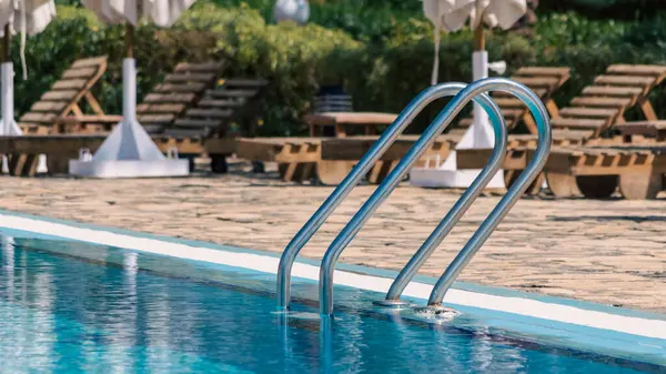 stock image handrails by the pool with blue water on the background of sun loungers and folded white umbrellas