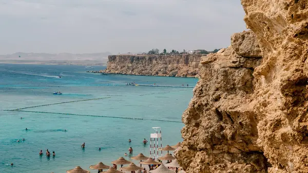 stock image view from the top of the beach with umbrellas of reeds boats and people standing in blue water on a partly cloudy day