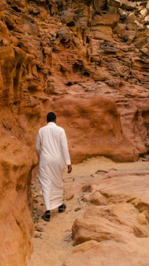 Beyaz Arap elbiseli bir adam renkli bir kanyonda yürüyor.