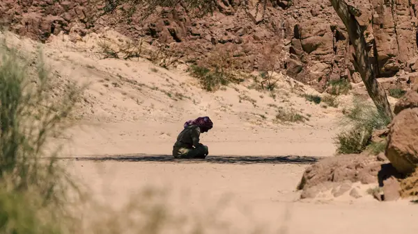 stock image Bedouin prays sitting on the sand in the shade of a tree in the desert against the backdrop of mountains