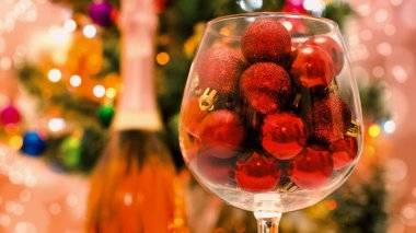 red glitter balls in a large wine glass close up against the background of a decorated green Christmas tree clipart