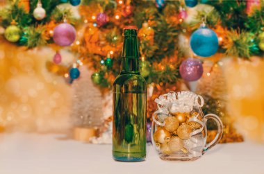 shiny yellow christmas balls in a beer glass next to a green bottle and a decorated new year tree clipart