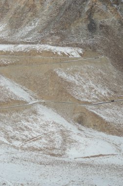Ladakh, Hindistan 'da kayalık bir dağ yamacını karlar kaplıyor. Bir yol üzerinden geçiyor. Bir kamyon görünürde, dağ büyüklüğünde cüce..