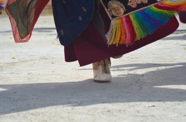 Ladakh, Hindistan 'da bir Budist tapınağında bir keşiş dans ediyor. Sadece ayağı, gölgesi ve bornozunun altı görünüyor. Onun ayakkabısı altın kaplamalı beyaz deri, onun kırmızı cübbesini renkli kumaşlar süsler..