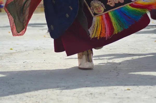 Ladakh, Hindistan 'da bir Budist tapınağında bir keşiş dans ediyor. Sadece ayağı, gölgesi ve bornozunun altı görünüyor. Onun ayakkabısı altın kaplamalı beyaz deri, onun kırmızı cübbesini renkli kumaşlar süsler..