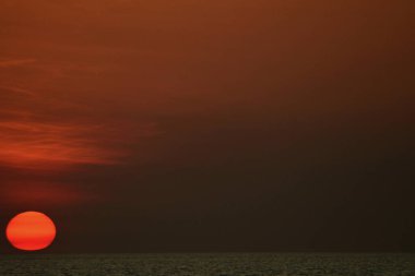 Güneş karanlık bir denize batıyor. Gökyüzünün geri kalanı karanlıkken, üzerindeki bulutlar koyu bir turuncudur. Güneş kırmızı şeritli canlı bir turuncudur..